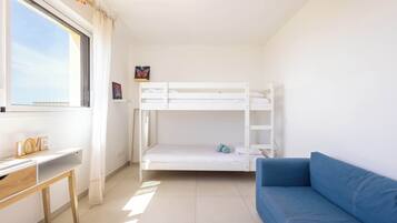 Una habitación con literas, un escritorio, un sofá azul y una ventana con cortinas.