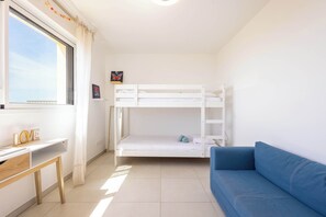 A room with a bunk bed, a desk, a blue sofa, and a window with curtains.