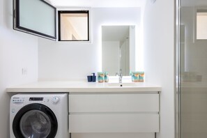 A modern bathroom with a white sink, a mirror, a washing machine, and a shower area. - Valras'Loc Archipel Capri – Sea View Escape (Valras-Plage)