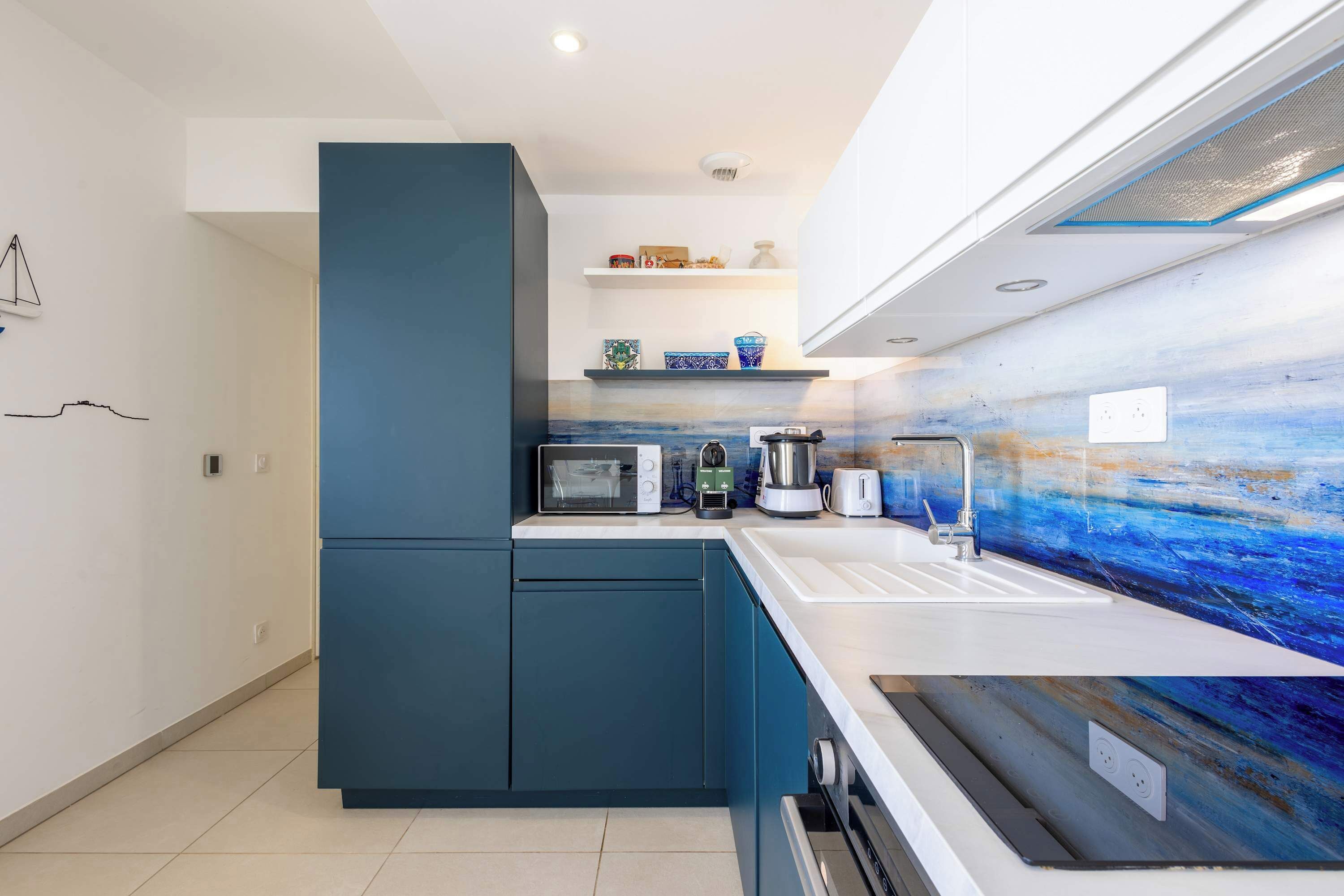 Een moderne keuken met een inbouwmagnetron, broodrooster, waterkoker en spoelbak. Er zijn kastjes en een aanrecht met een blauwe achterwand.