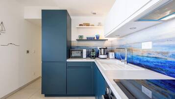 Een moderne keuken met een inbouwmagnetron, broodrooster, waterkoker en spoelbak. Er zijn kastjes en een aanrecht met een blauwe achterwand.