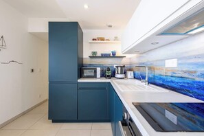 A modern kitchen with a built-in microwave, toaster, kettle, and sink. There are cabinets and a countertop with a blue backsplash.