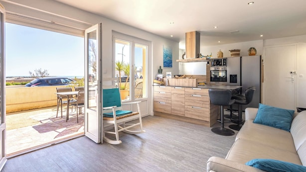 A modern kitchen with a dining area, a sofa, and a view of the outdoors.