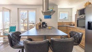 A modern kitchen with a central island, black leather chairs, stainless steel appliances, and a view of the outdoors.