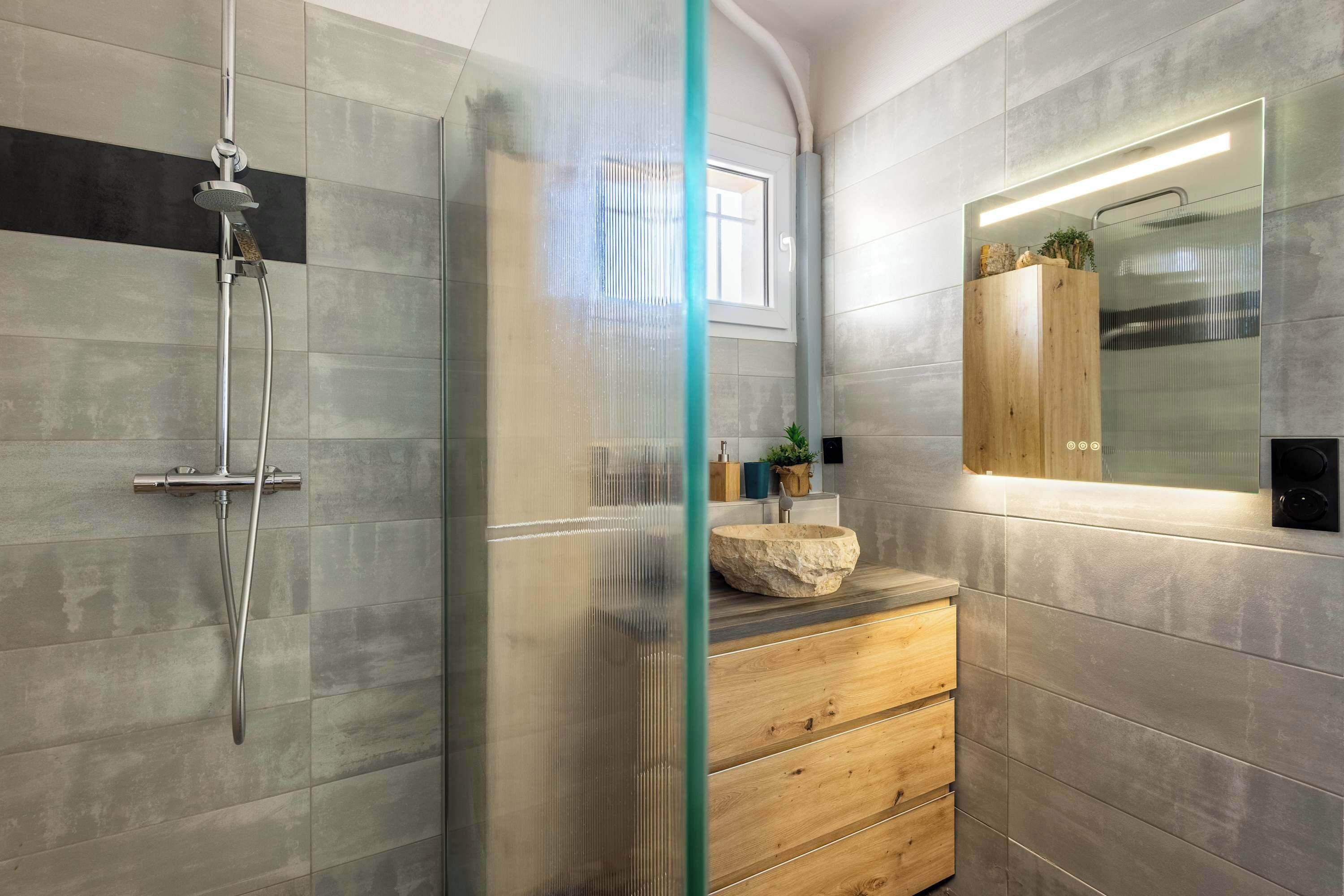 Ein modernes Badezimmer mit Duschkabine aus Glas, einem Holzkosmetikschrank und einem großen Spiegel.