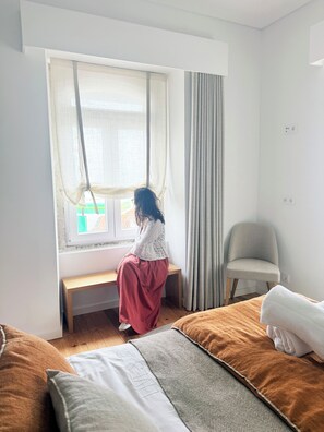 Une pièce comprenant un lit, un banc, une chaise et une fenêtre avec des rideaux.