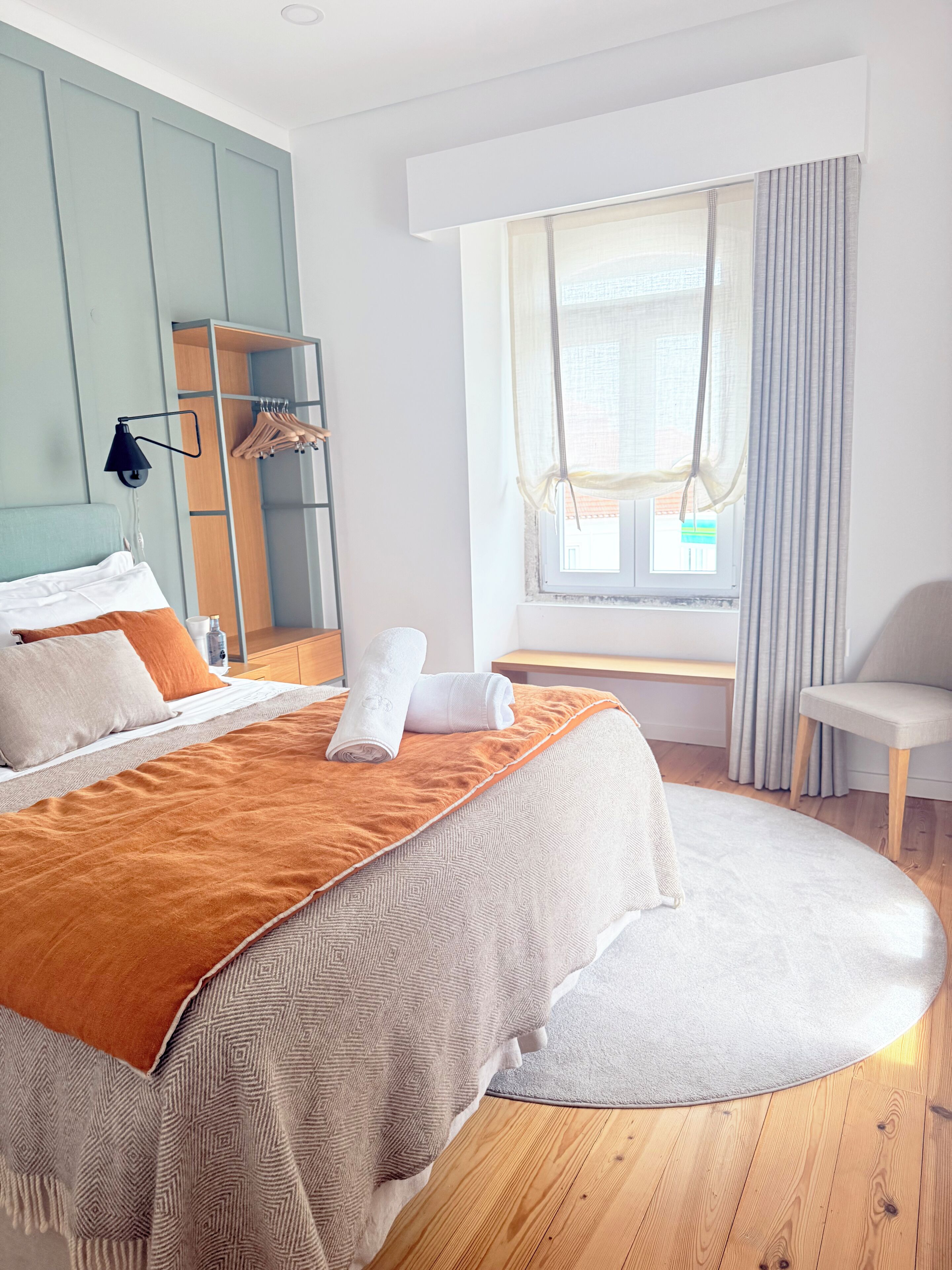 Una habitación de hotel moderna con una cama, zona de estar, ventana con cortinas y suelo de madera.