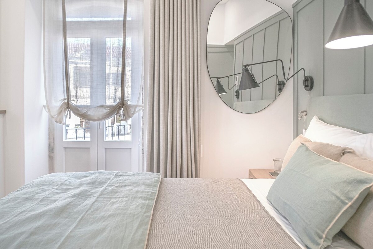 A bedroom with a bed, a hanging chair, a mirror, and a bedside table.