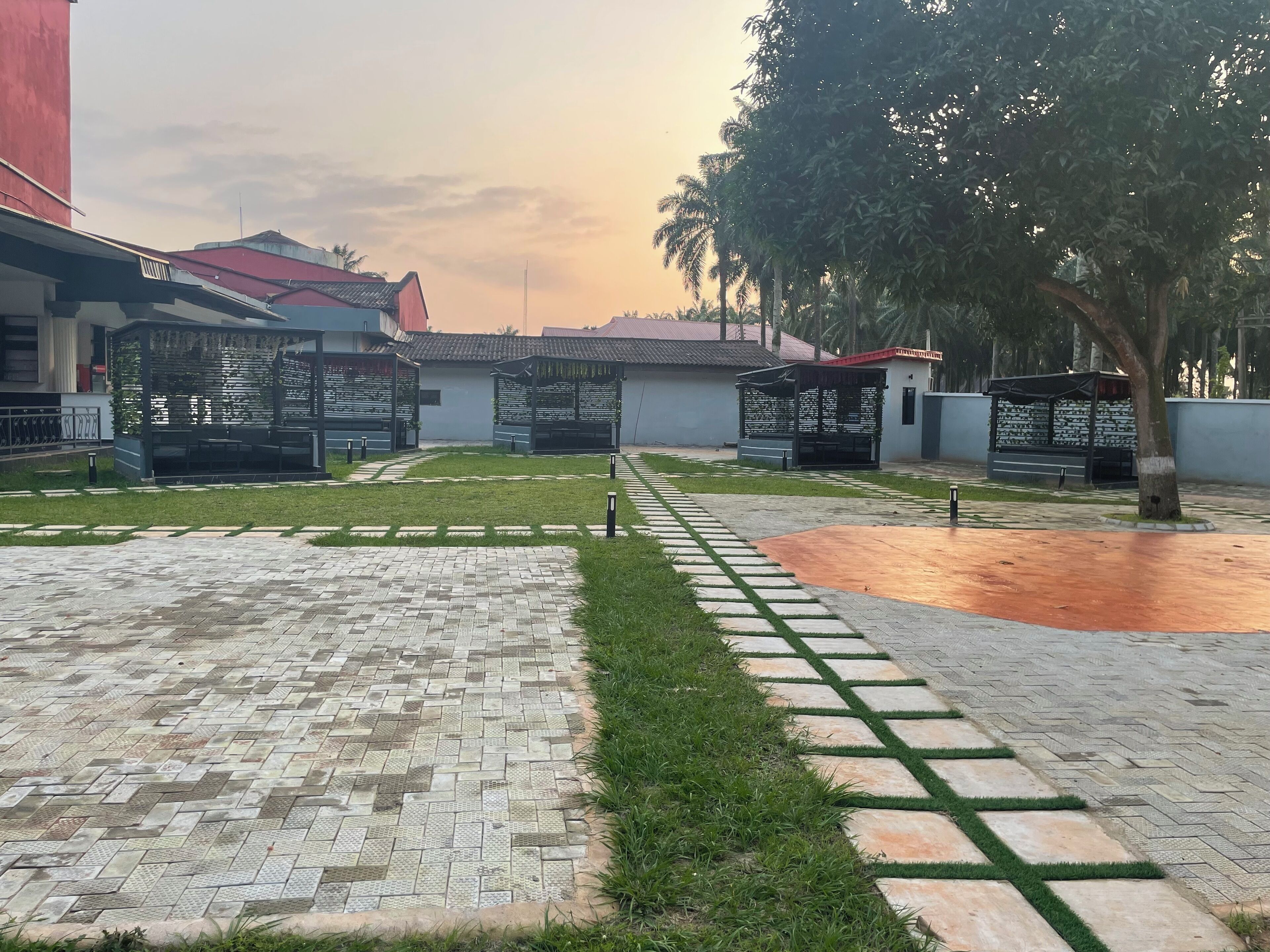 Pátio com piso estampado, grama verde e pequenas construções com inscrições.
