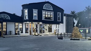 Un edificio de dos pisos con fachada oscura y detalles blancos, que cuenta con ventanas grandes y una entrada central con escalones.