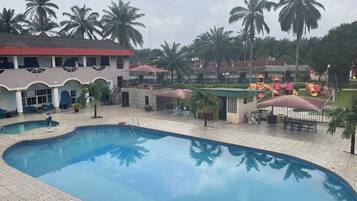 A swimming pool with a tiled deck, surrounded by palm trees and a playground with slides and play structures.