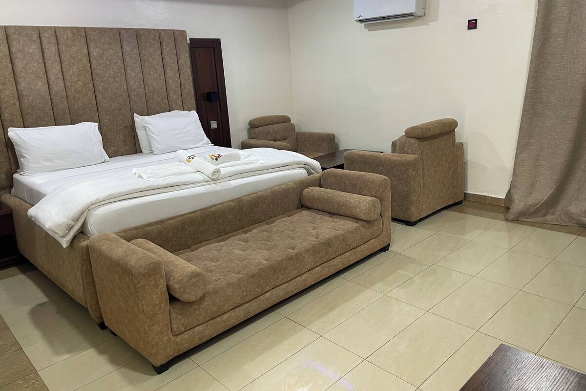 Ein modernes Hotelzimmer mit einem großen Bett, zwei Sesseln, einem kleinen Tisch und einer Klimaanlage an der Wand.