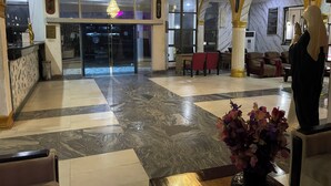 Vestíbulo de hotel con piso de mármol, mostrador de recepción, candelabro y sillas rojas.