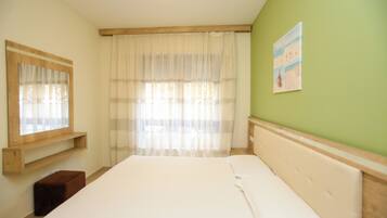 A bedroom with a bed, a window with sheer curtains, a wooden headboard, and a green wall.