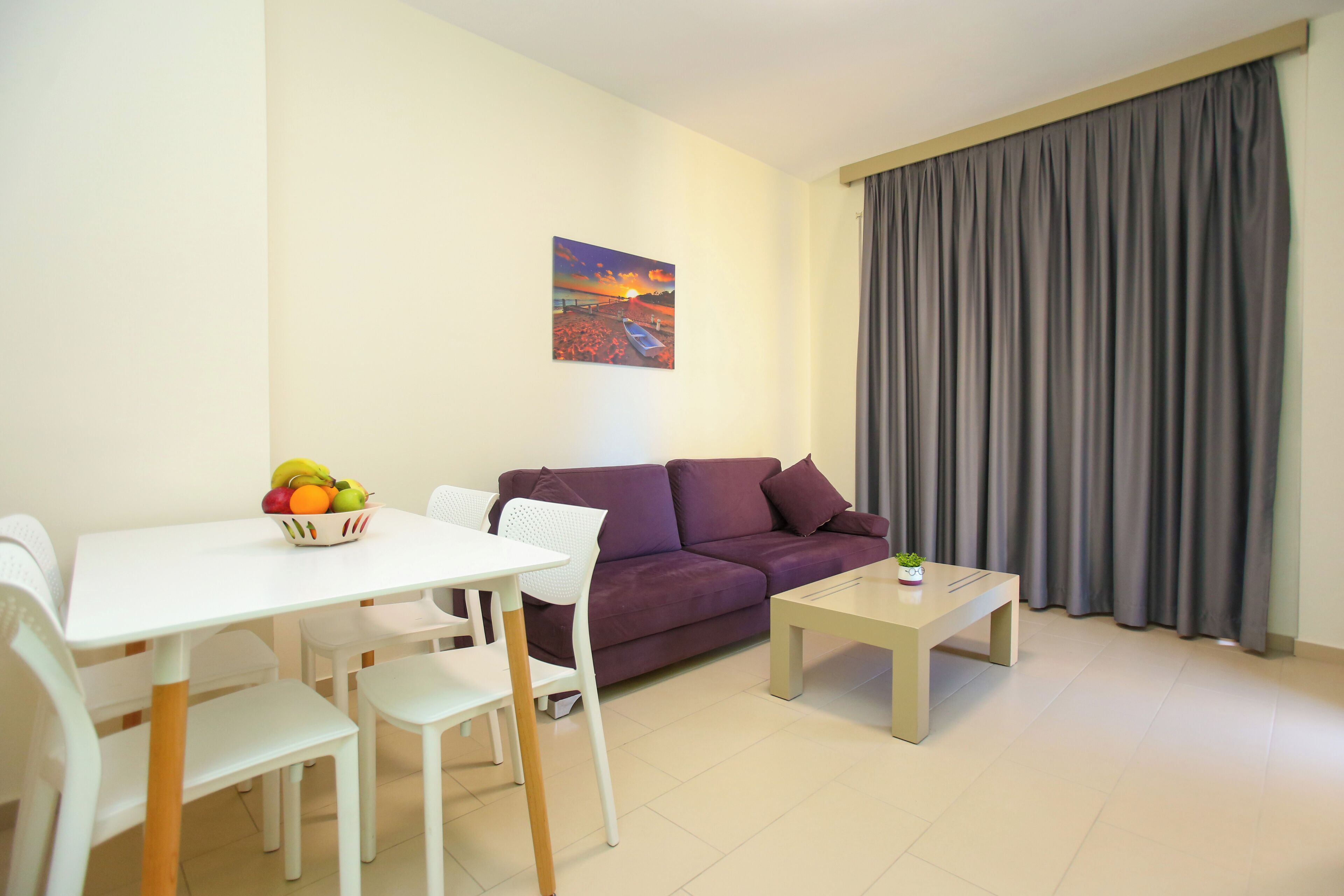 A modern living room with a white dining table, purple sofa, and a painting on the wall.