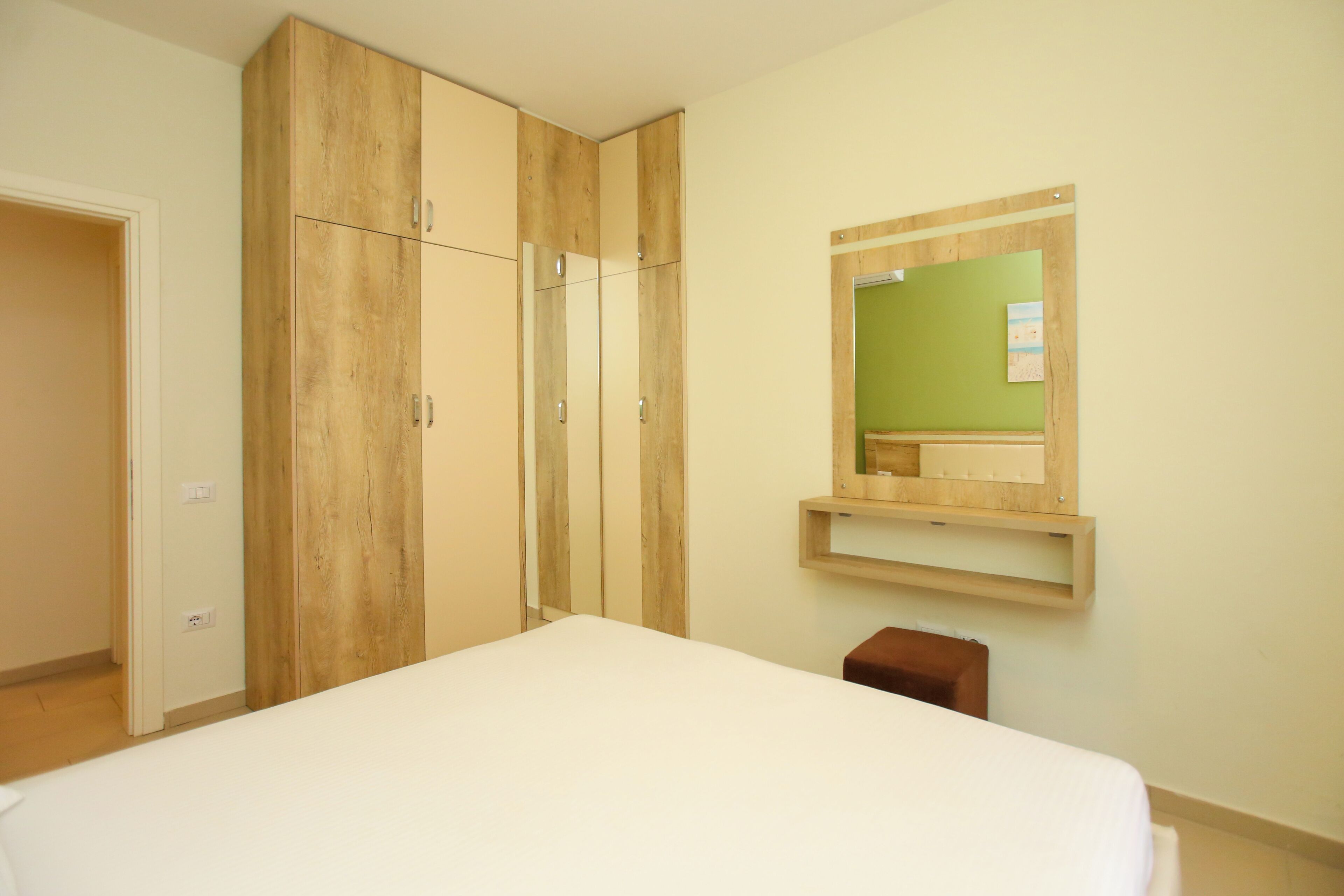 Ein Schlafzimmer mit Bett, Kleiderschrank, Spiegel und einem kleinen Hocker.