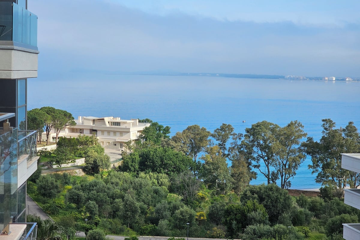 Une vue sur la côte, avec un bâtiment moderne, une végétation luxuriante et une mer bleue et limpide.