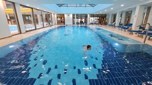 Una piscina interior con agua cristalina, rodeada de sillones de descanso y un techo de cristal.
