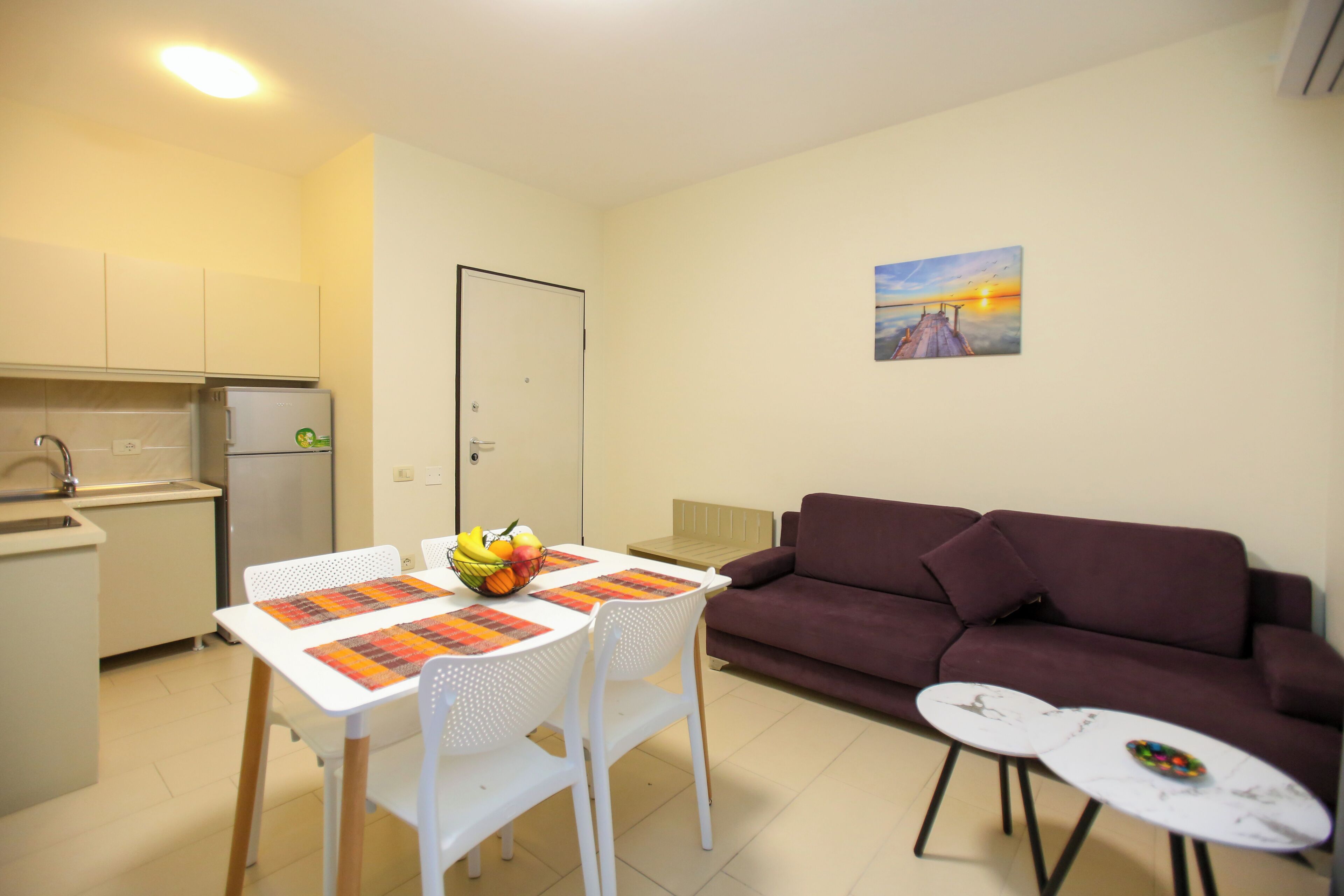 A compact living space with a kitchenette, a dining table with chairs, a purple sofa, and a small side table.