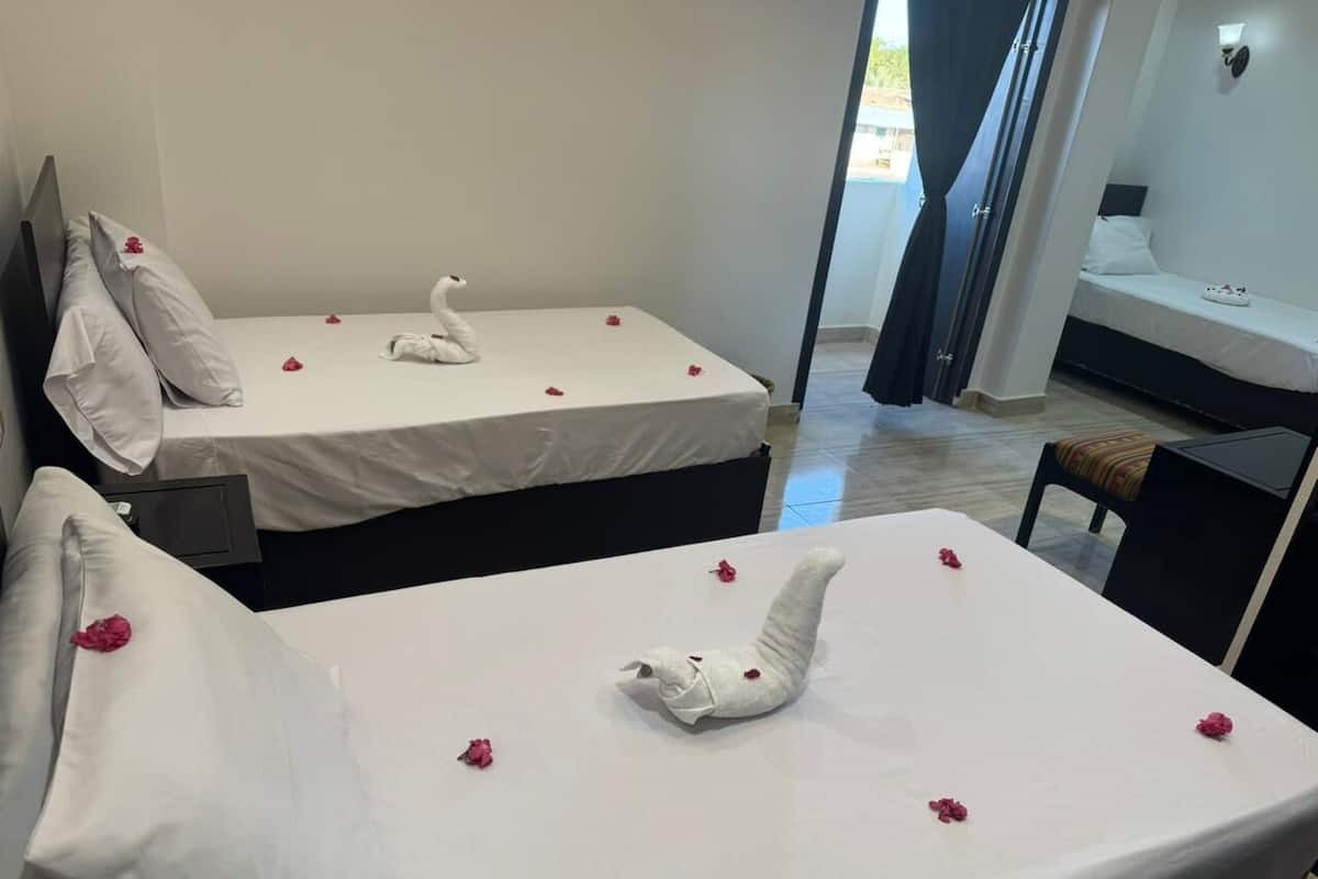 Habitación de hotel con dos camas, cada una decorada con una toalla con forma de cisne y pétalos de rosa esparcidos.