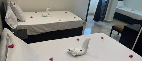 A hotel room with two beds, each adorned with a swan-shaped towel and scattered rose petals.