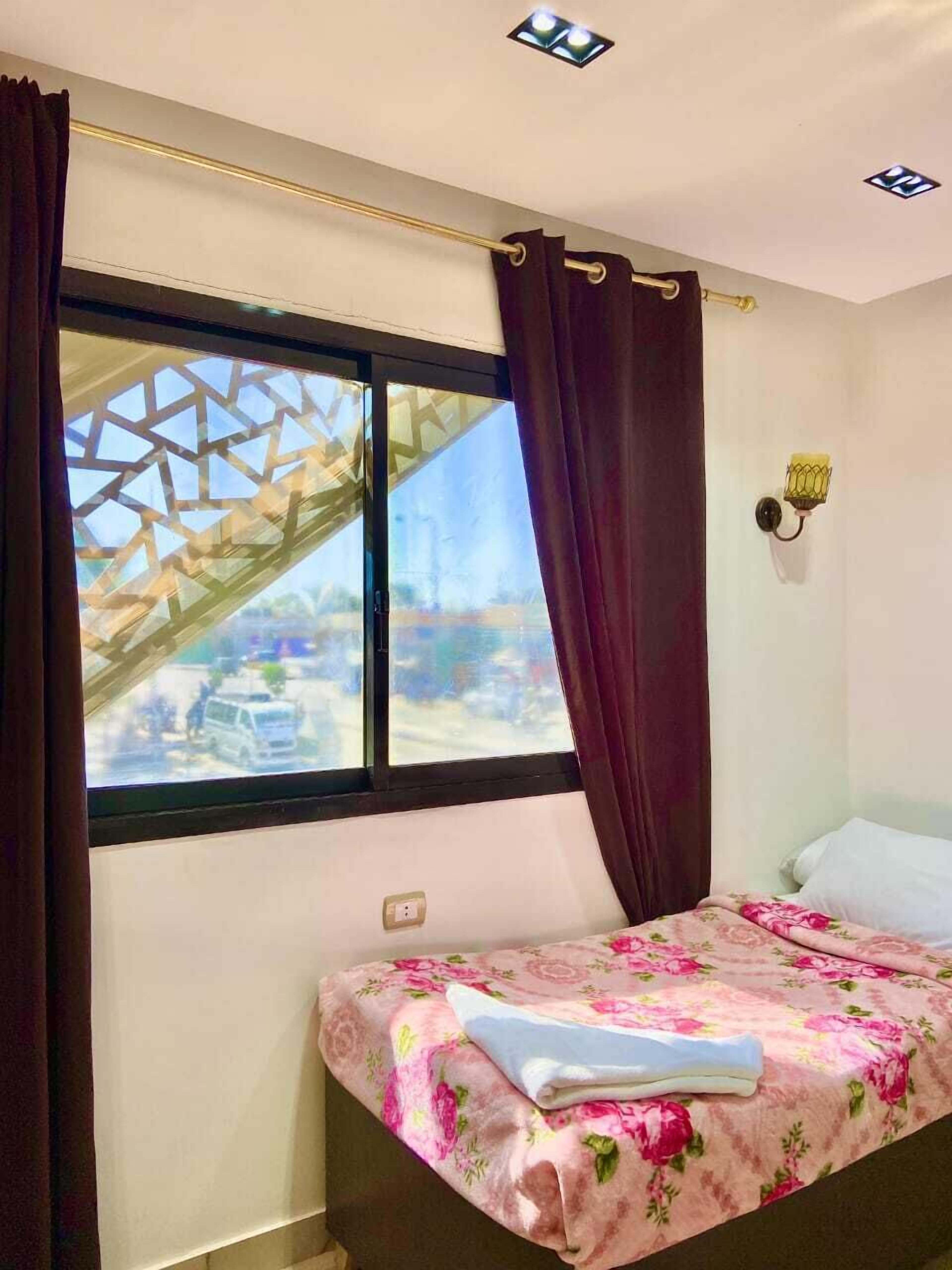 Ein Schlafzimmer mit Bett, einem Vorhangfenster, einer Wandleuchte und Blick ins Freie.