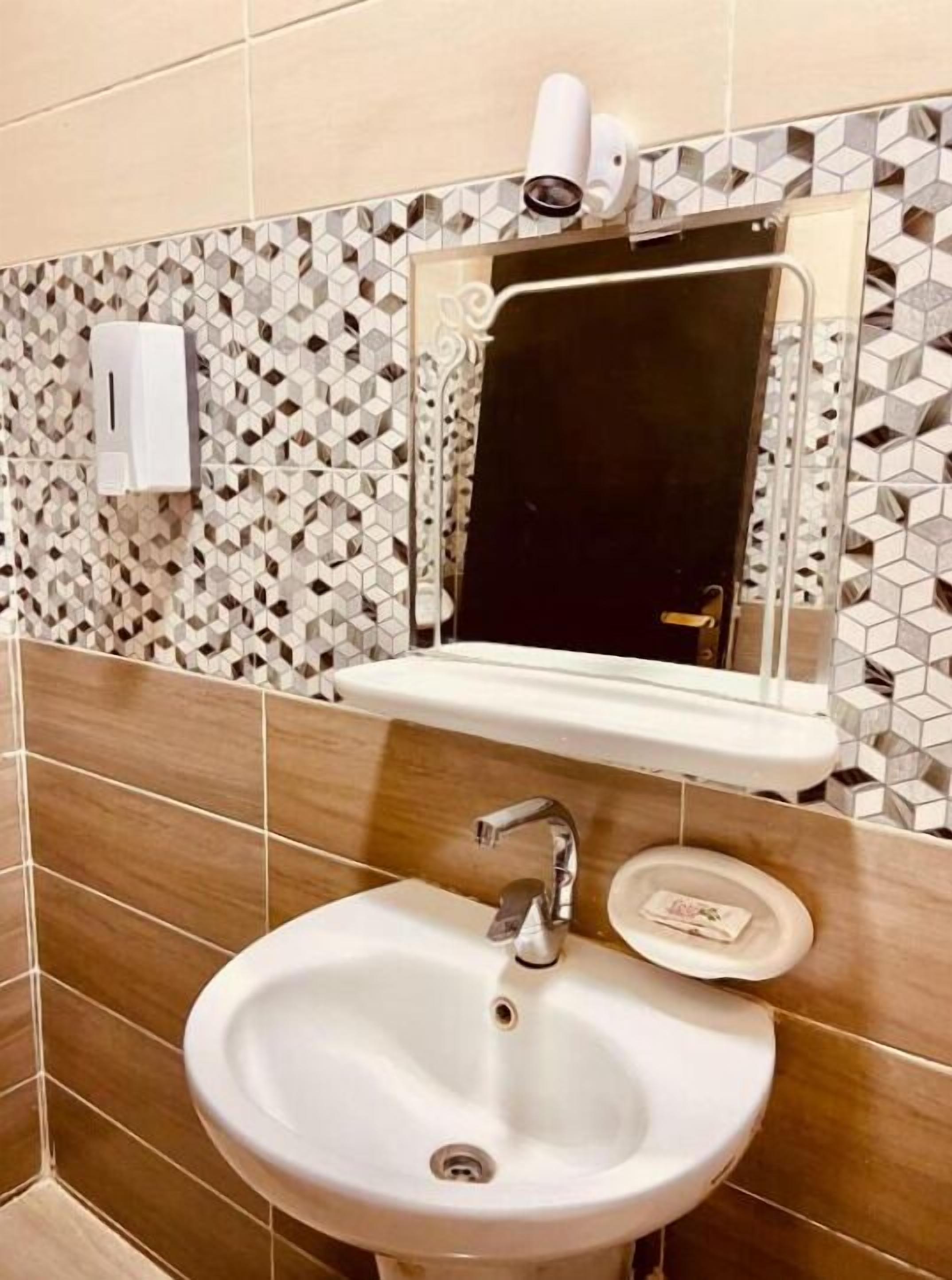 Un baño con lavamanos, espejo y dispensador de jabón.
