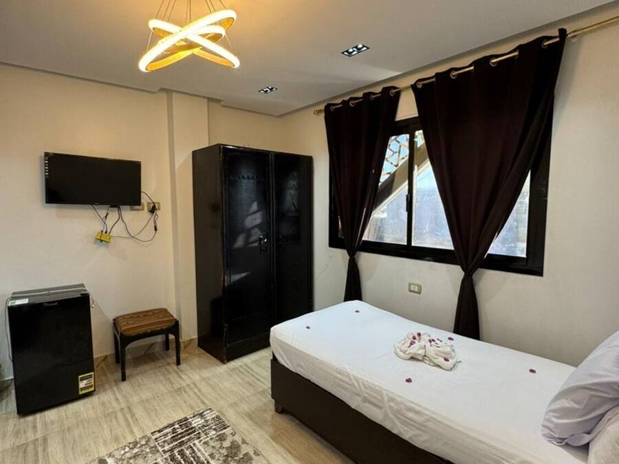 Un dormitorio con cama, televisión, armario, escritorio y alfombra.