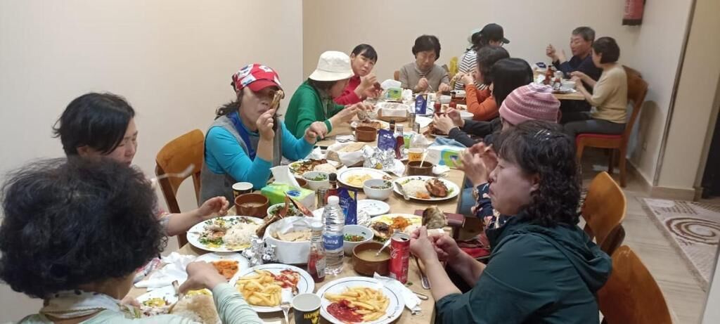 Un grupo de personas sentadas alrededor de una mesa con diferentes platos, sugiriendo un ambiente de comida compartida.