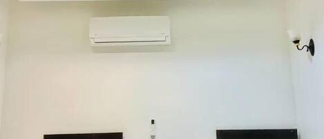 A hotel room with two beds, a ceiling light fixture, an air conditioning unit, and a small black speaker.