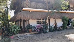 Un edificio con techo de paja y balcón de madera, rodeado de plantas en macetas y suelo de grava.