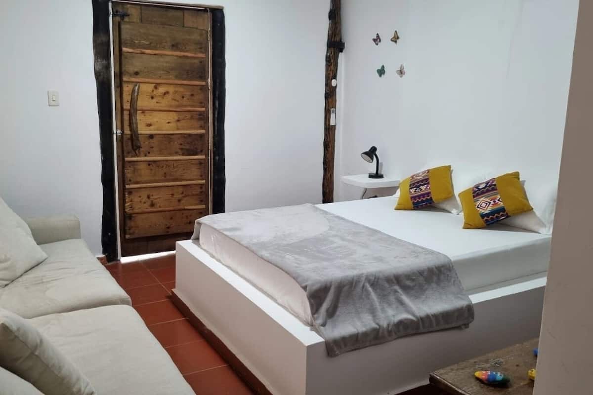 A bedroom with a bed, a sofa, a small table, and a wooden door.