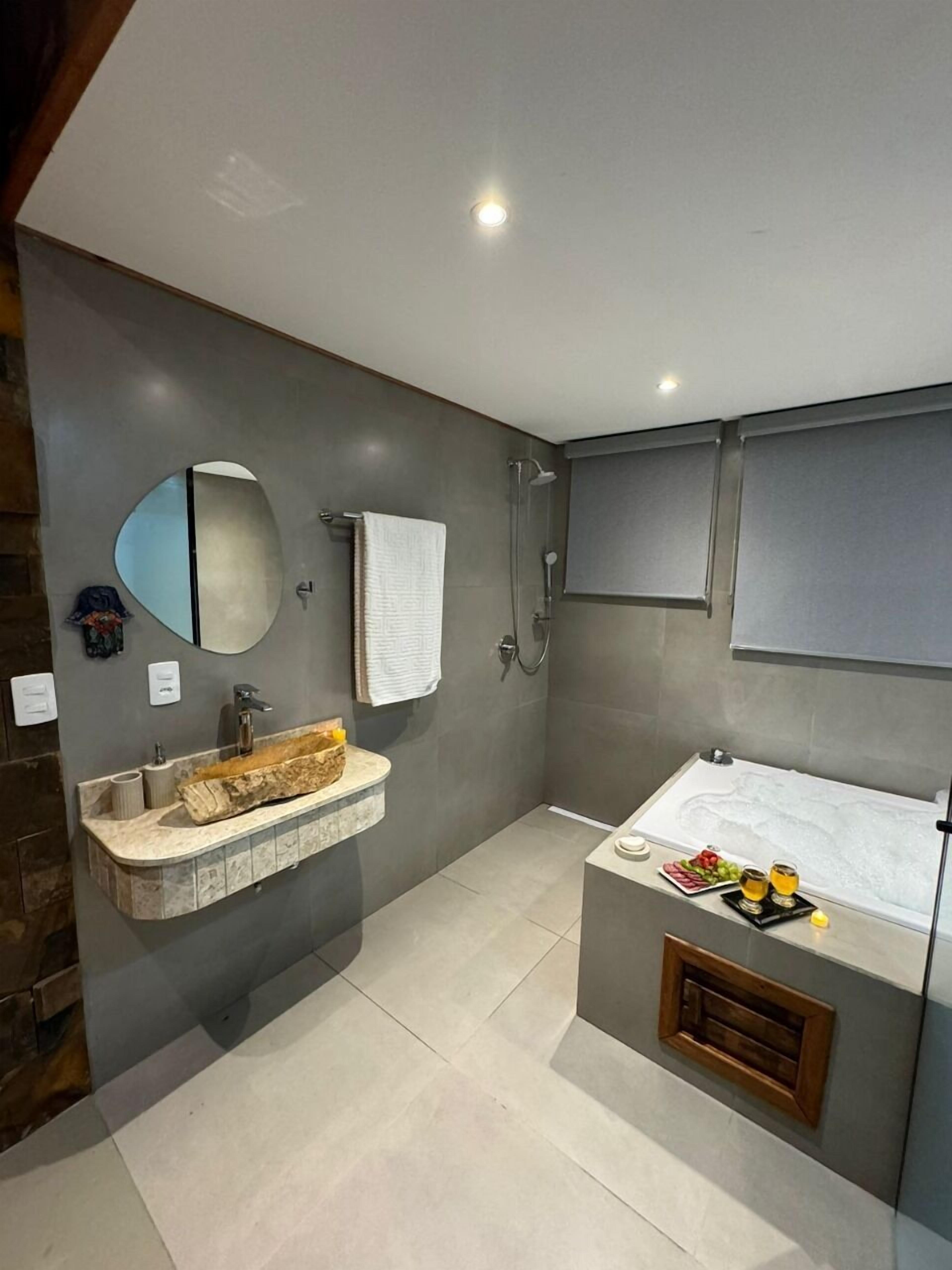 Uma casa de banho moderna com lavatório de mármore, um espelho grande, chuveiro e banheira.