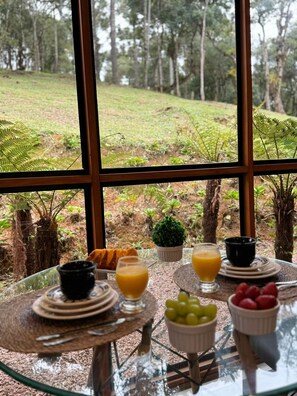 A breakfast table with fruit, juice, and a view of a forest through large windows. - Pousada Refugio Arauca (Campo Alegre)