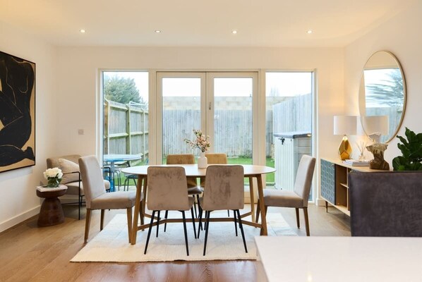 Enjoy meals in this dining area with a round table and six chairs, surrounded by a large window and lush greenery.