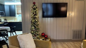 Uma sala de estar com sofá, mesa de centro, TV fixada na parede e árvore de Natal.
