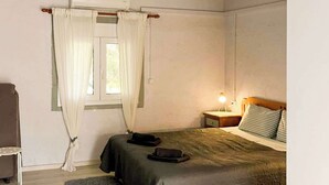 A small, single-bed room with a desk, chair, and a window with curtains.