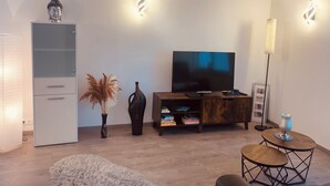 Un salon moderne avec un téléviseur à écran plat, un meuble, un vase contenant de l’herbe des pampas et une petite table ronde avec une lampe.