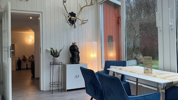 Un intérieur moderne comprenant un coin repas, une plante en pot, une statue de lion décorative et une grande fenêtre donnant sur des arbres.