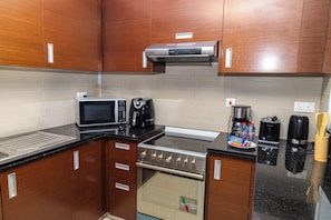 A compact kitchen with a microwave, toaster, coffee maker, and a stove.