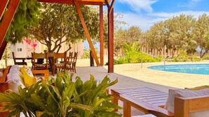 A covered outdoor seating area with a pool in the background. - Spondylus Bungalow (Canoas)