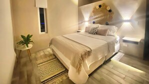 A bedroom with a bed, a small table with a plant, a decorative wall piece, and a window. - Spondylus Bungalow (Canoas)