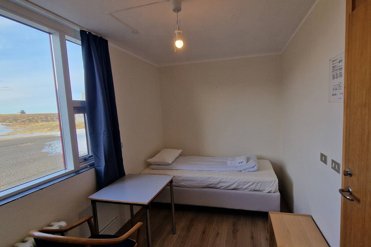 A small, single-bed room with a window, a desk, and a chair.