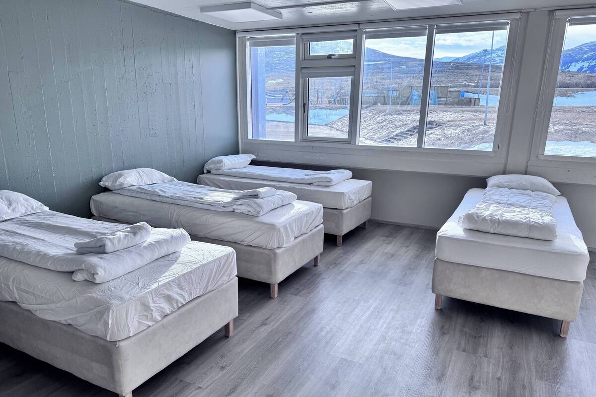 A room with four beds arranged in a row, large windows with a view of a snowy landscape, and wooden flooring.