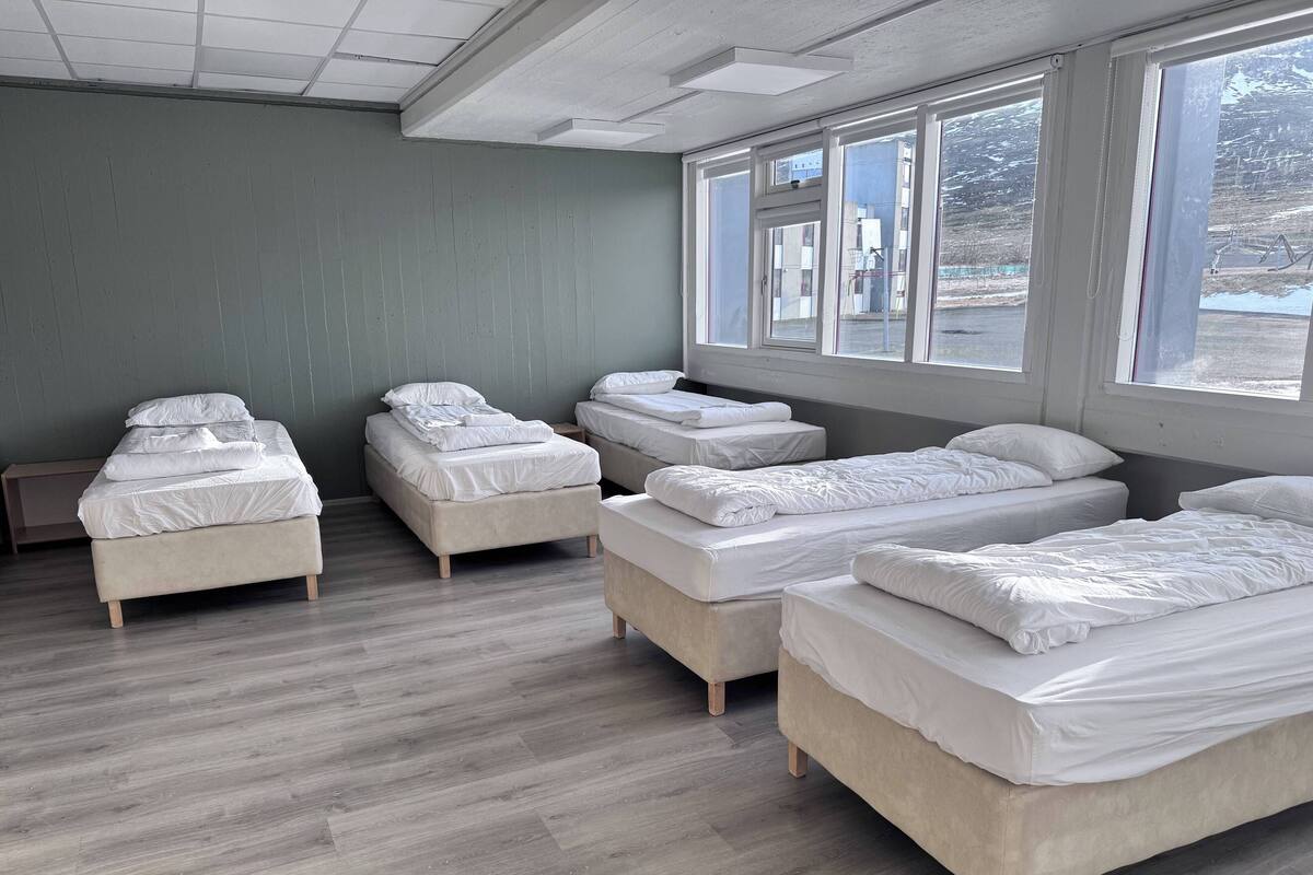 A hotel room with four beds arranged in a row, large windows, and a wooden floor.