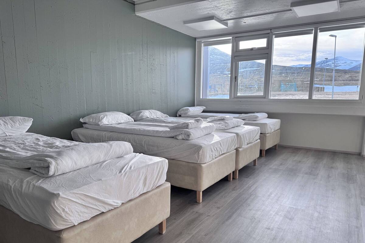A hotel room with a large window, multiple beds, and a light-colored wooden floor.