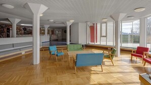 A spacious indoor area with wooden flooring, multiple seating arrangements, and large windows allowing natural light. - Hunavellir Guesthouse (Blönduós)