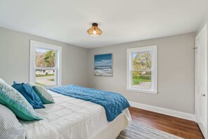 A bedroom with a bed, two windows, a painting, and a ceiling light.