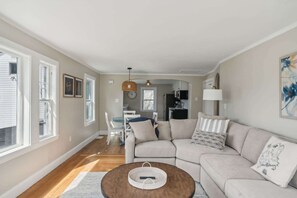 A living room with a beige sofa, a coffee table, and a dining area with a table and chairs.