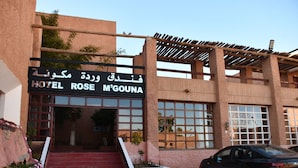 Een hotel ingang met een bord waarop 'HOTEL ROSE M'GOUNA' staat en een auto die ervoor geparkeerd staat.